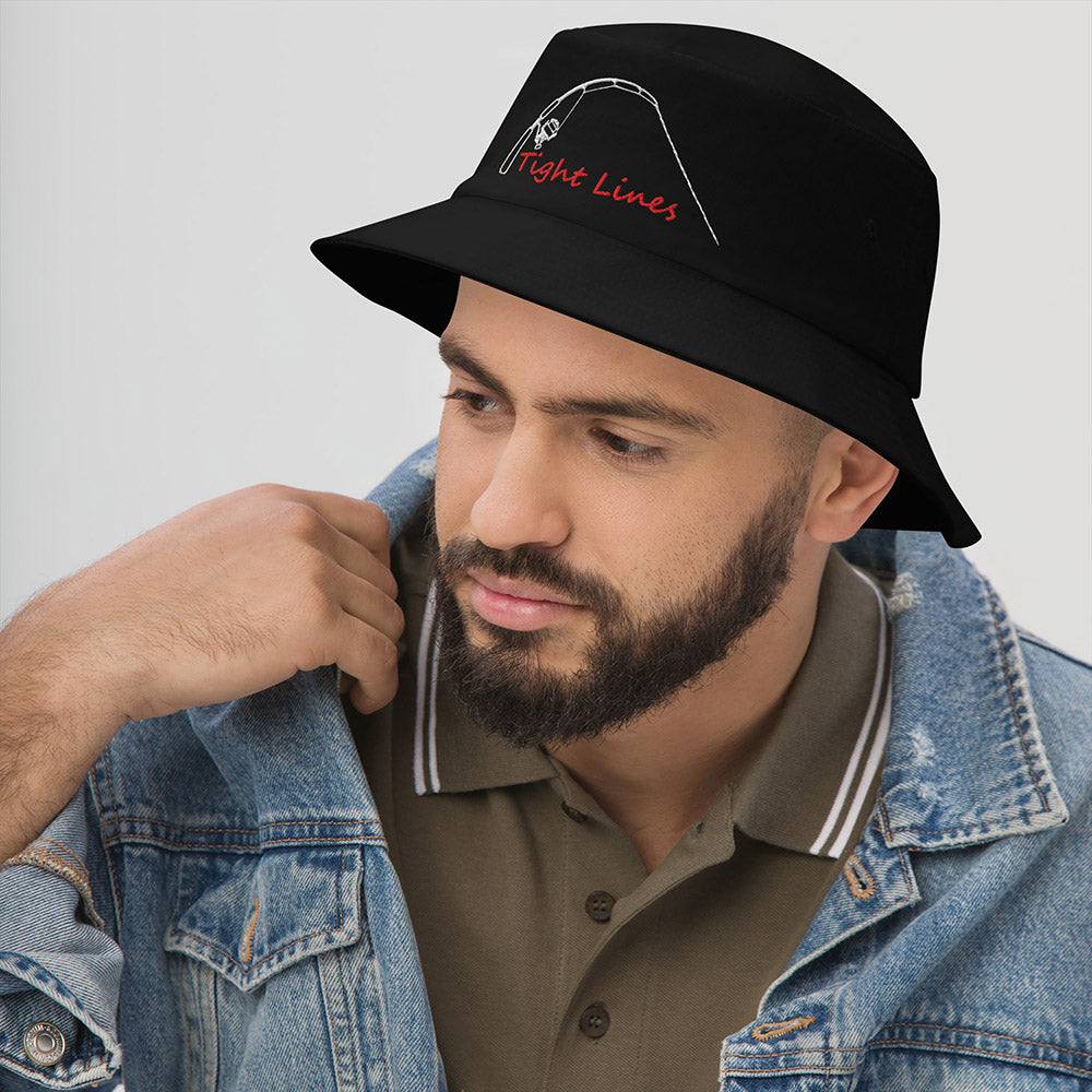 Black fishing bucket hat with embroidered 'Tight Lines' rod and reel design, shown on male model in denim jacket