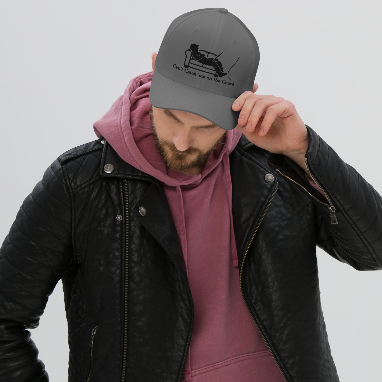 Man wearing dark grey dad hat with fisherman couch design, adjusting brim, maroon hoodie and black jacket