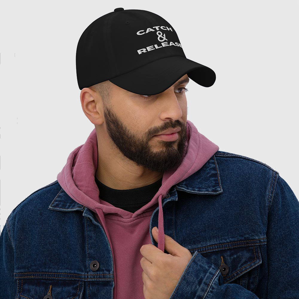 Man in denim jacket and hoodie wearing black dad hat with Catch & Release slogan