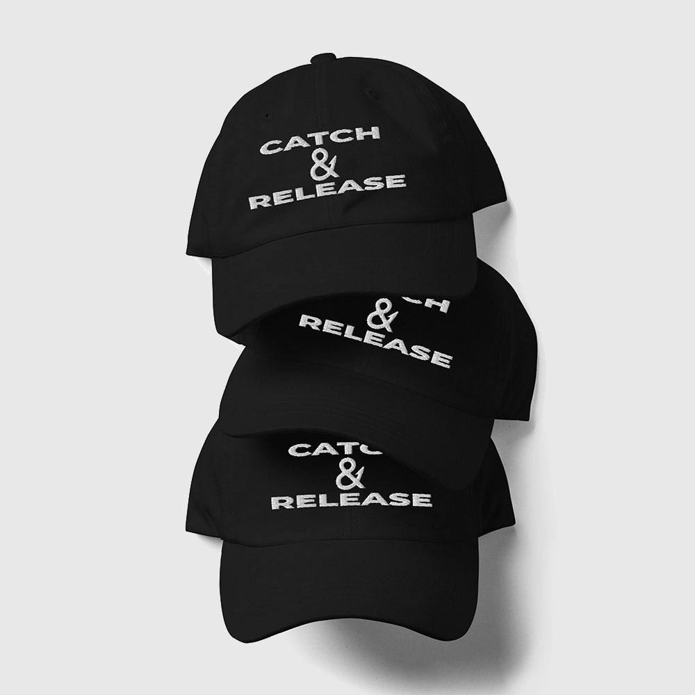 Three stacked black Catch & Release dad hats with white text