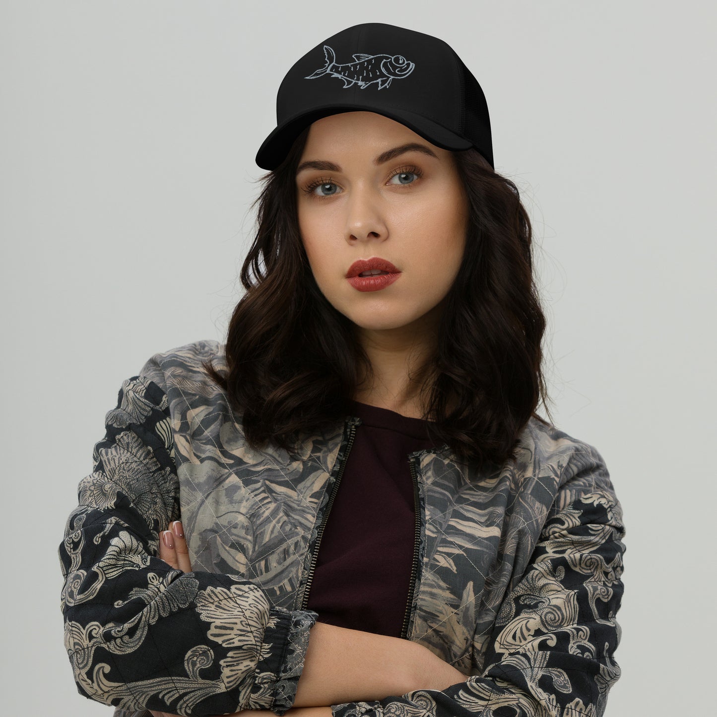 Woman wearing black trucker hat with embroidered tarpon design.