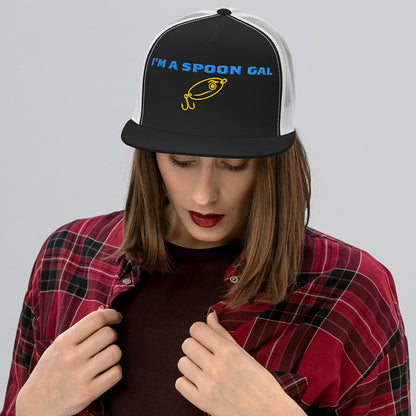 Black and white trucker fishing hat with blue "I’m a Spoon Gal" text and yellow lure graphic, worn by woman. - Spoon Gal Trucker Hat