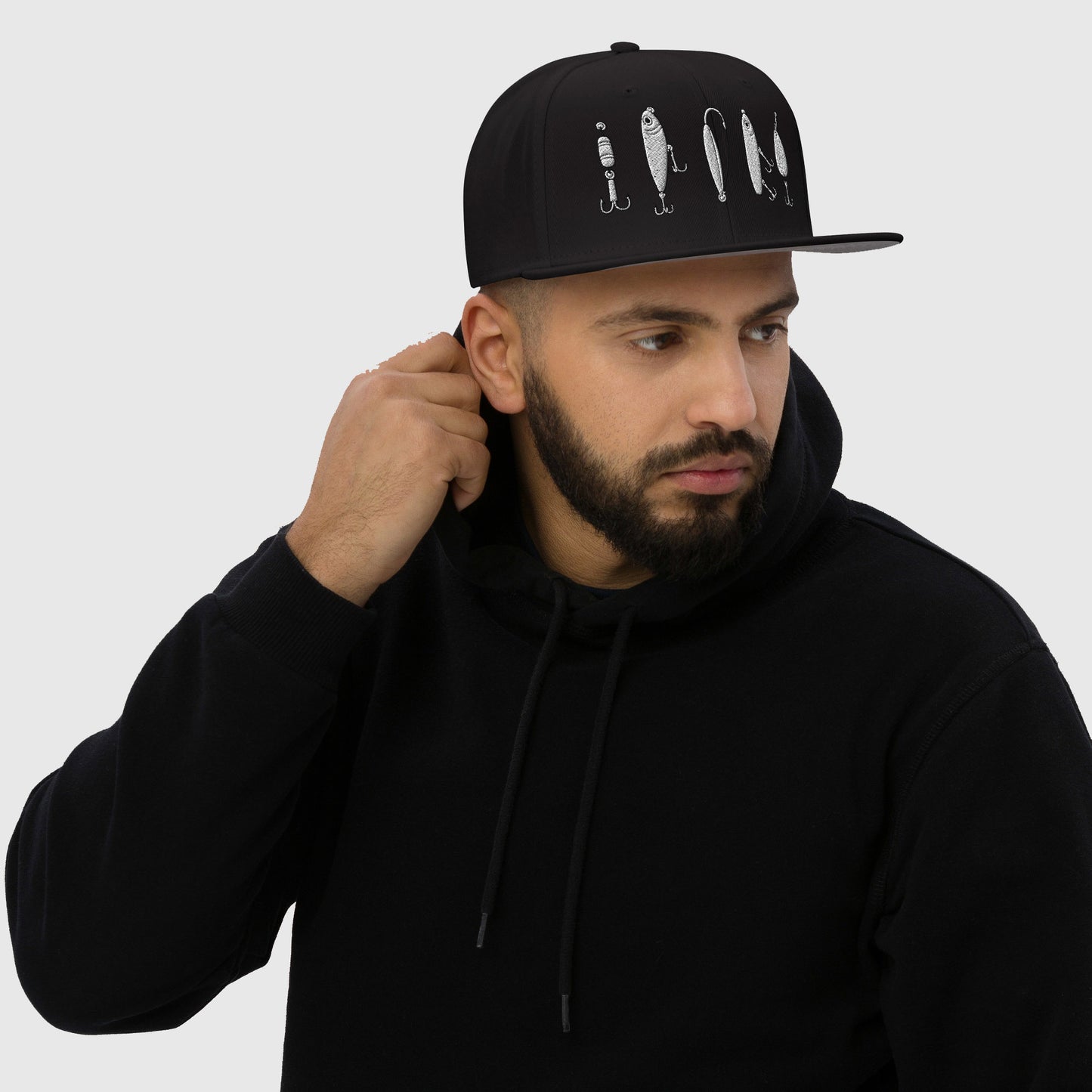Man in black hoodie adjusting black snapback with lure design