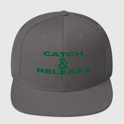 Dark grey snapback fishing hat with green "Catch & Release" text embroidery, flat brim design. - Catch & Release Snapback