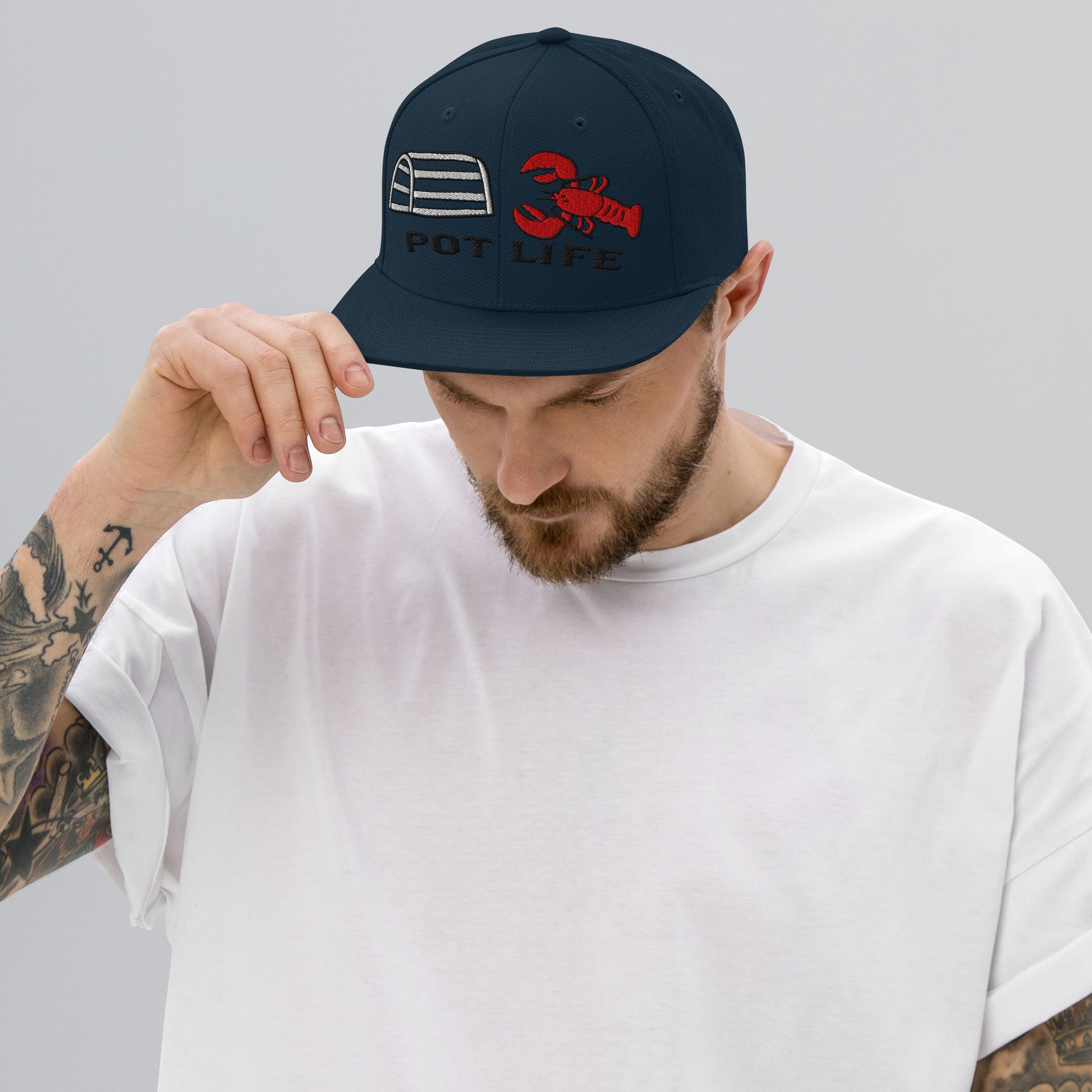Man wearing a dark navy snapback with embroidered lobster trap, red lobster, and “POT LIFE” text