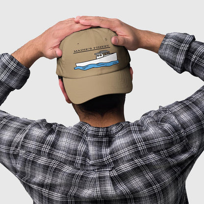 Khaki fishing hat with "Maine's Finest" lobster boat graphic and adjustable strap, worn by person. - “Maine’s Finest” Lobster Boat Dad Hat