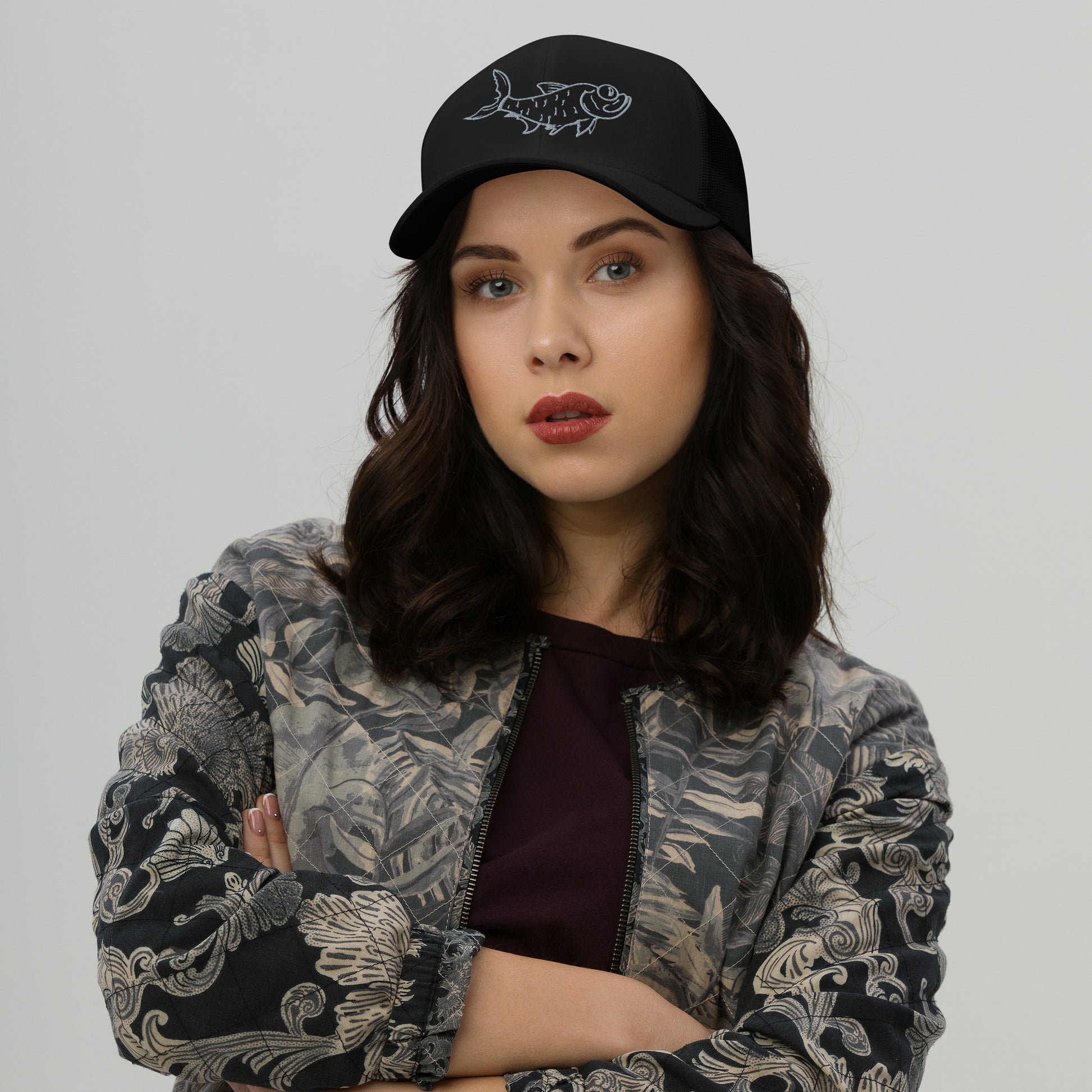 Woman wearing black trucker hat with embroidered tarpon design.